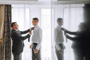 Two men are getting dressed up, one of them is wearing a tie photo