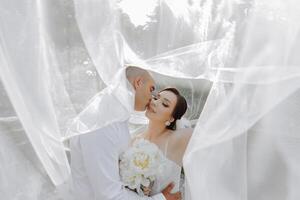 A bride and groom are kissing in front of a white curtain photo