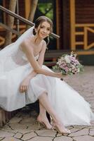 A bride is sitting on a stone staircase with a bouquet of flowers in her hand photo