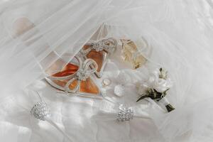 A pair of shoes with a bow on them are on a bed with a bouquet of flowers photo