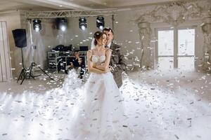 A bride and groom are dancing in a room with confetti falling around them photo