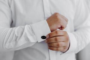 A man is getting dressed in a white shirt and black cufflinks photo