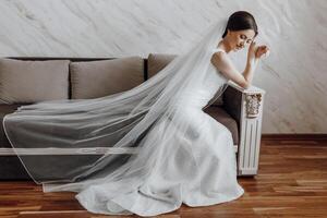 A woman in a white dress is sitting on a couch with a veil draped over her head photo