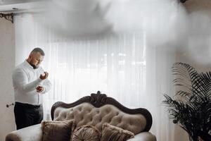 A man is getting dressed in front of a couch photo