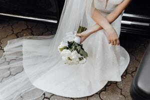 A bride is sitting in a car with a bouquet of flowers in her lap photo