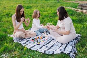 A woman sits on a blanket with two children, painting photo