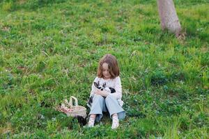 A young girl sits in a grassy field holding a rabbit in her arms photo