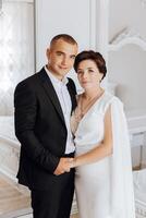 A man and woman are posing for a picture in a room with a bed in the background photo