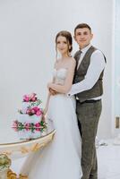 A bride and groom stand in front of a wedding cake photo