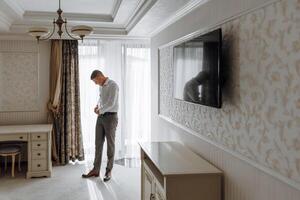 A man is getting dressed in a room with a large mirror on the wall photo