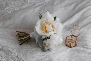 A bouquet of white flowers sits on a bed next to a small gold box photo