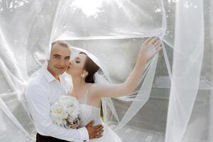A bride and groom are hugging in front of a white veil photo