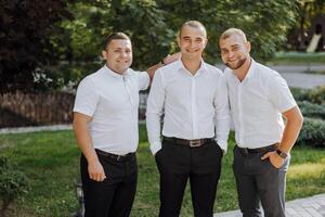 Tres hombres en blanco camisas y negro pantalones son posando para un foto