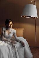 A woman in a white dress sits on a couch in front of a lamp photo