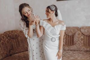 Two women are sitting on a couch, one of them is wearing a wedding dress photo