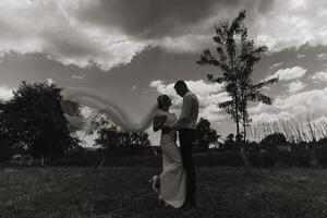 A couple is standing in a field with a tree behind them photo