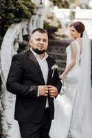 A man in a black suit is standing on a staircase with a woman in a white dress photo