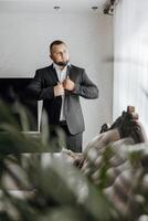 A man in a suit is getting dressed in front of a couch photo