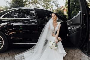 A woman in a wedding dress sits in the back of a black car photo