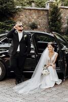 A man and a woman are posing for a picture in front of a black car photo