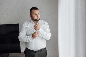 A man in a white shirt is getting dressed in front of a window photo