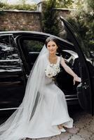 A woman in a wedding dress is sitting in the back of a black car photo