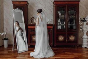 A woman in a white dress stands in front of a mirror, looking at her reflection photo