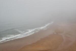 Foggy beach with waves and walkers photo