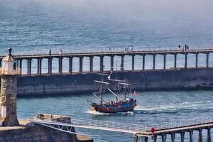 Historic sailing ship in harbor with pier and lighthouse in Whitby, North Yorkshire photo