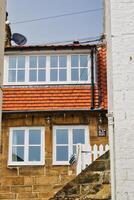 encantador dos pisos casa con tejas rojas techo y enmarcado en blanco ventanas Robin capucha bahía, Yorkshire foto