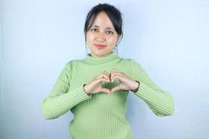 Smiling young asian woman making a heart gesture with her fingers in front of her chest photo