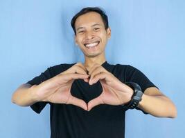 handsome asian man is making a heart shape symbol with his fingers. love and romantic concept. photo