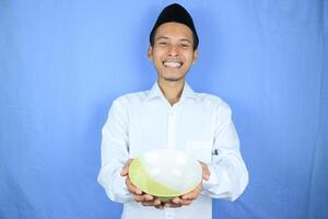 Muslim Asian man wearing cap stand and hold an empty bowl and spoon showing the dish photo