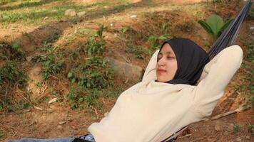 young muslim woman with headscarf sleeping in hammock on deck terrace during sunny summer afternoon. photo