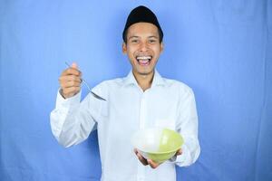 Muslim Asian man wearing cap stand and hold an empty bowl and spoon showing the dish photo