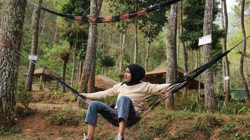 Pensive smiling young woman with headscarf resting in comfortable hammock at green garden. photo