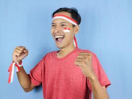 Excited expression young indonesian man wearing red and white headband with clenching fist gesture. photo