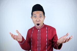 Surprised young Asian Muslim man looking camera, reacting ramadan news on white background photo