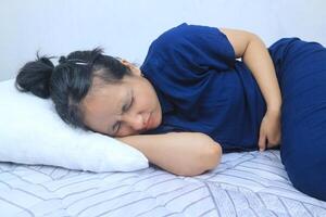 Beautiful asian young woman lying on bed and holding hands on her stomach. Menstrual period concept photo