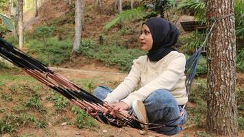 Pensive smiling young woman with headscarf resting in comfortable hammock at green garden. photo