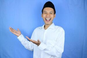 Smiling expression of muslim asian man, presenting and showing an empty space. Advertising concept photo