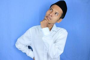 Confuse expression of asian muslim man doing thinking gesture, looking for idea on white background photo