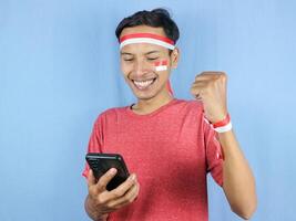 Excited expression young indonesian man celebrate indonesian independence day while holding phone. photo