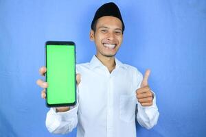 Smiling happy of muslim asian man wearing cap showing empty phone screen. Advertising concept photo