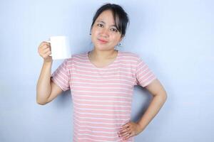 smiling expression of young asian woman looking at the camera while showing white cup, isolated on white background photo