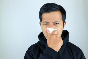 Sad and unhappy asian man suffering from fever and flu, blowing his nose and sneezing into tissue photo