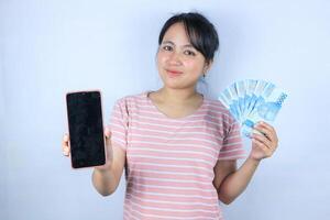 smiling expression of asian woman holding cash rupiah and showing empty mobile screen. photo