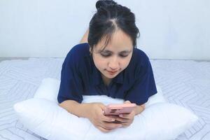 beautiful asian woman using mobile phone, browsing social media on smart phone while lying in bed photo