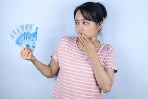 surprise expression asian woman covering her mouth while holding cash rupiah. Advertisement concept photo