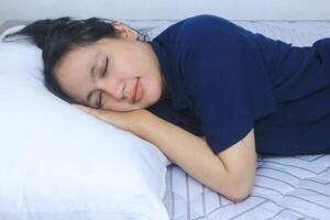 hermosa asiático mujer duerme cómodamente y dulce Sueños acostado en cama en acogedor dormitorio foto